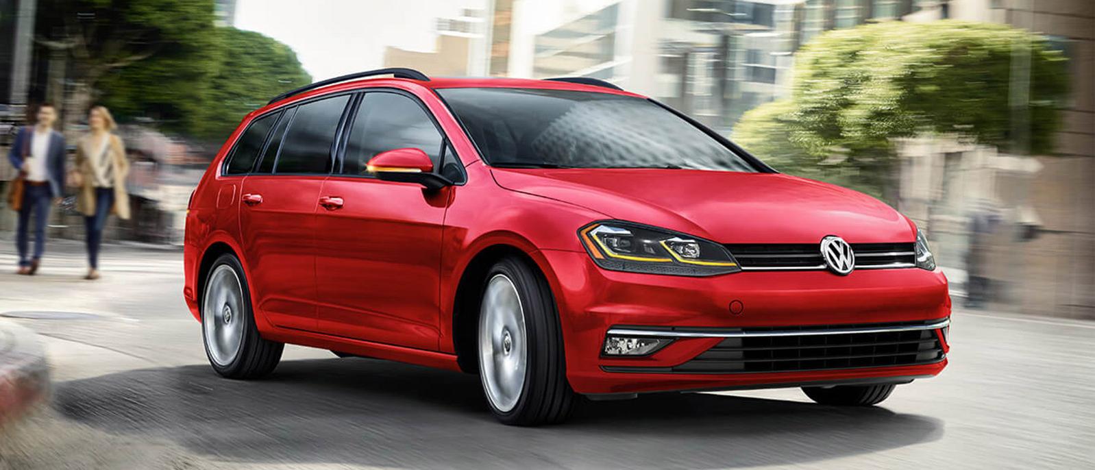 A red Volkswagen Golf SportWagen driving around a city street corner. A red Volkswagen Golf SportWagen driving around a city street corner.