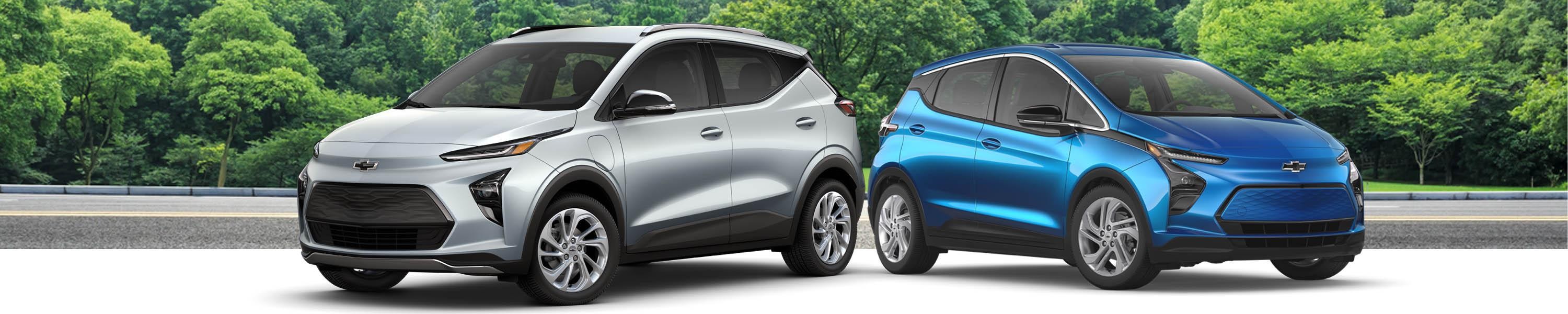 A Chevrolet Bolt EV and Bolt EUV parked with a forest background behind it.