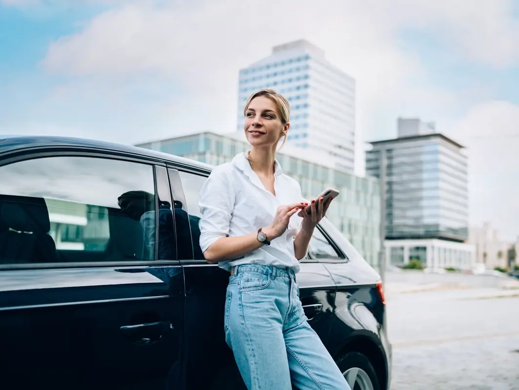 Woman standing next to car smiling while on her phone