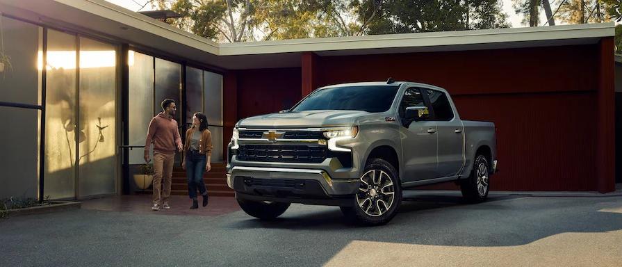 A silver 2022 chevrolet silverado parked on a driveway with people nearby