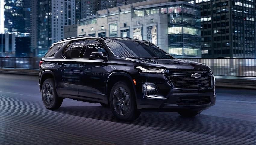 New 2023 Chevy Traverse Midnight Edition driving in a lit up city landscape