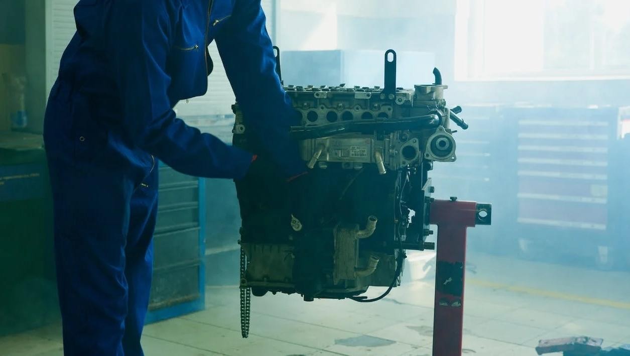 Engine being worked on by a mechanic in a garage with blue overalls on