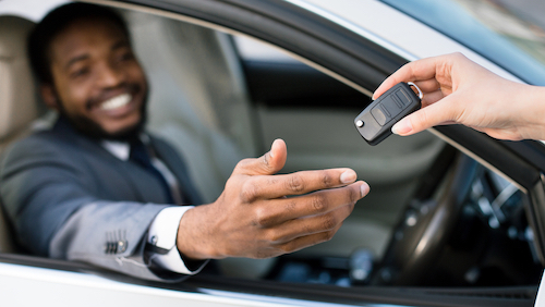 Salesperson handing keys to smiling African American car buyer