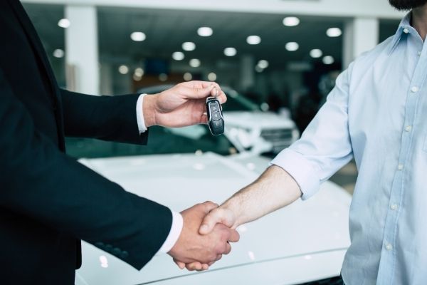 Two men shaking hands while one presents the other a key to a new vehicle