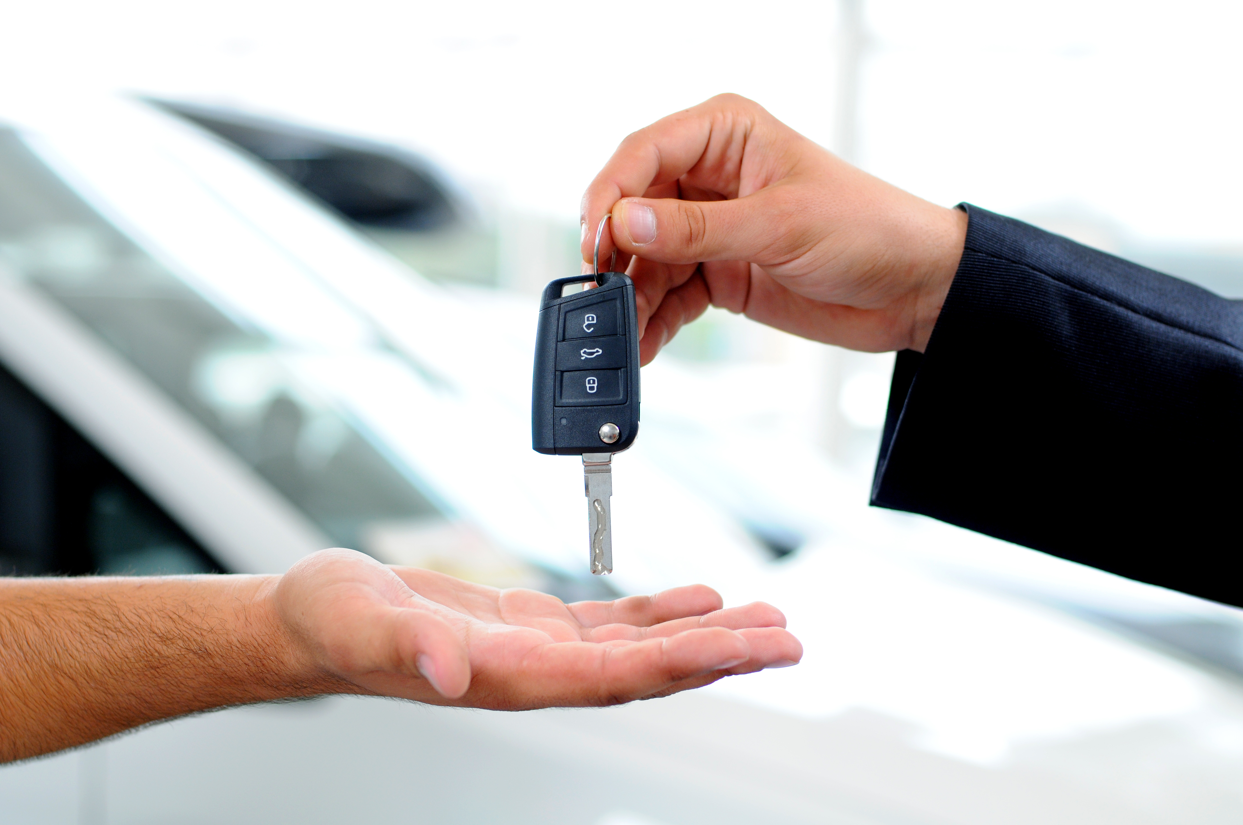 Two men shaking hands while one presents the other a key to a new vehicle