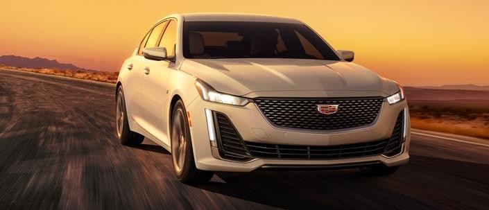 Cadillac 2024 CT5 Premium Luxury in Summit White with Sahara Beige interior and 18" alloy with Diamond Cut Android Gloss finish wheels 7/8 passenger side front view; sunset;
