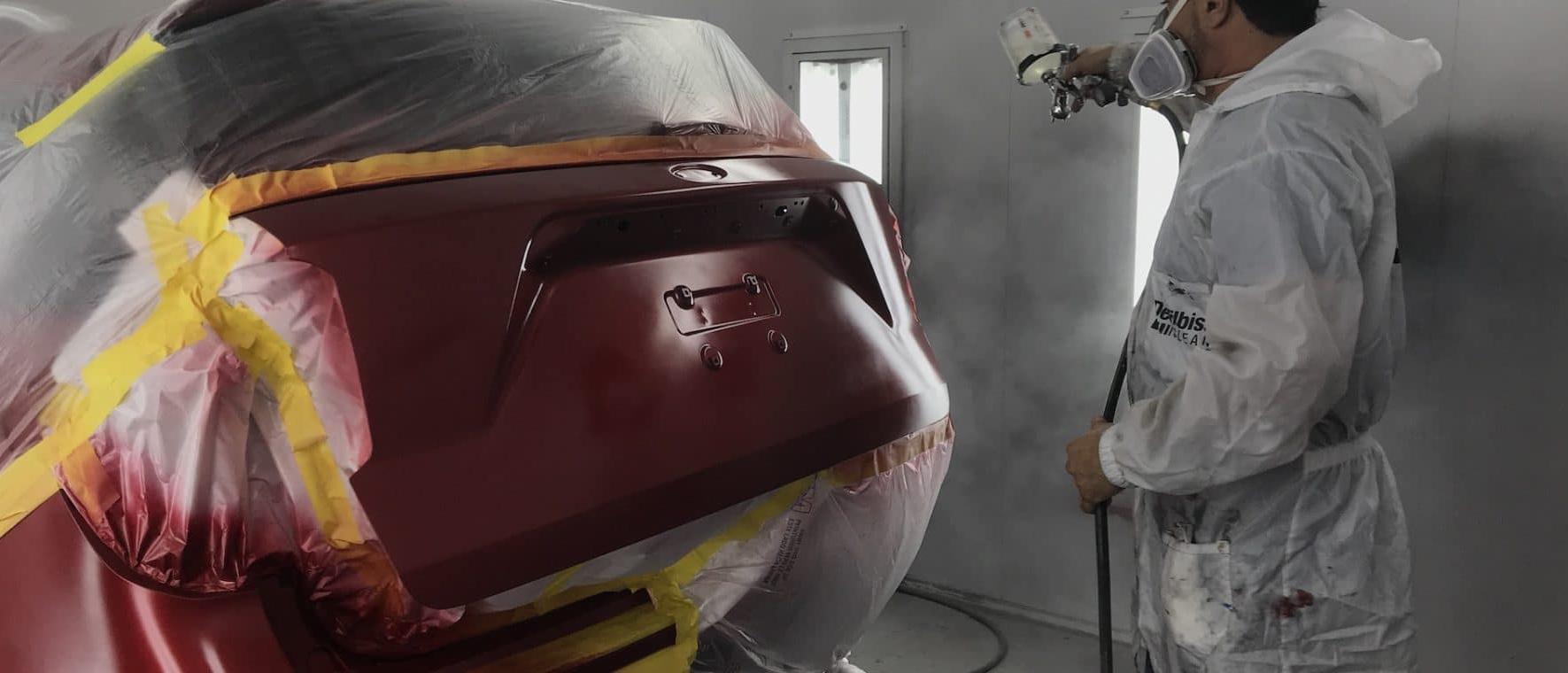 Technician spray painting vehicle