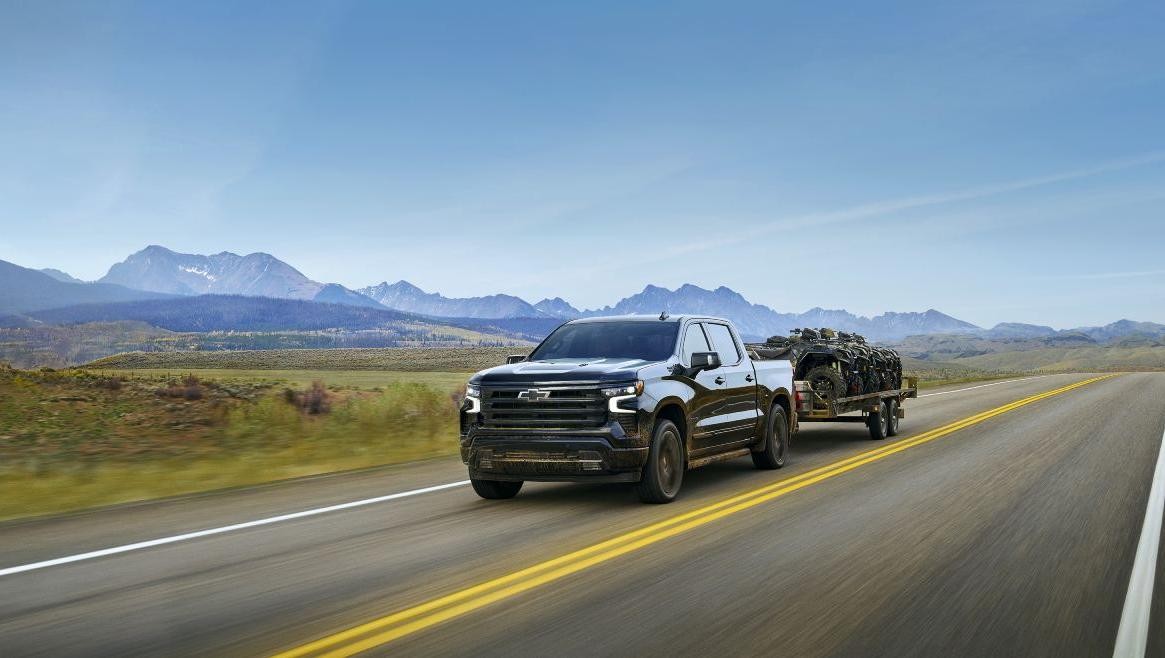 2025 Chevy Silverado 1500 towing a trailer down a country road