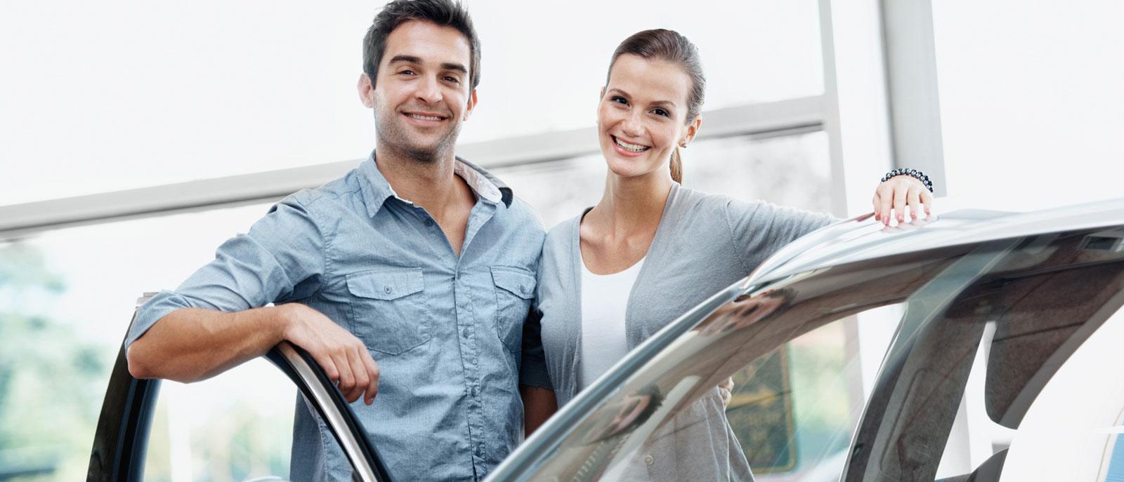 Smiling couple in a dealership standing besides a new vehicle