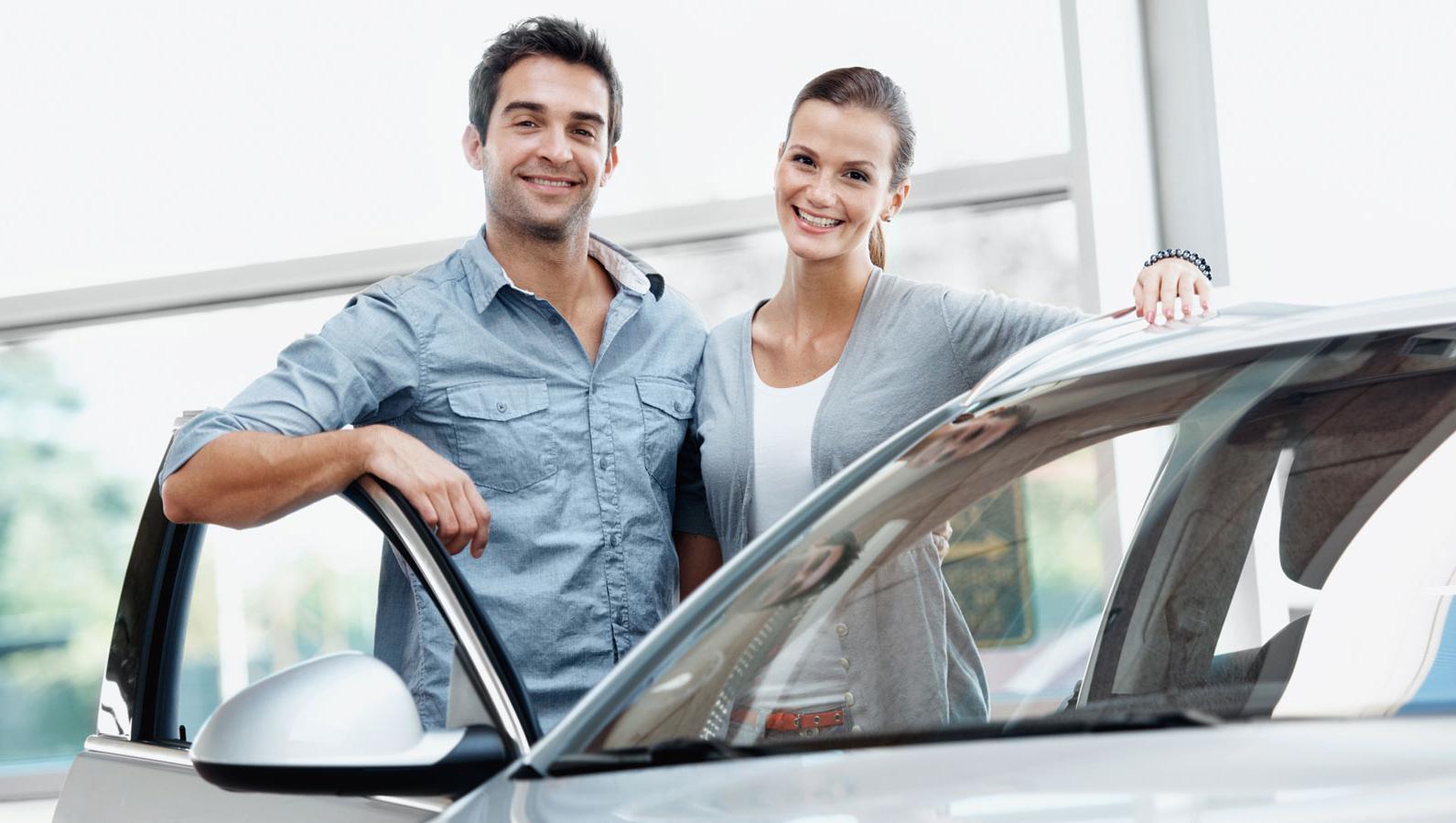 Smiling couple in a dealership standing besides a new vehicle