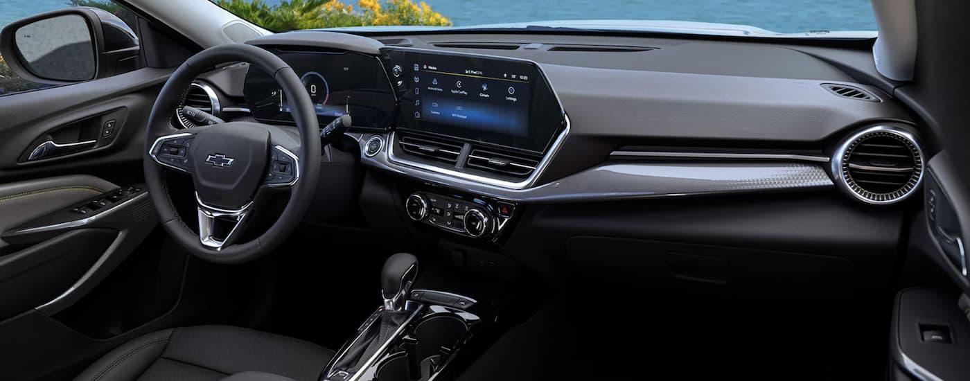 The black interior of a 2024 Chevy Trax shows the steering wheel and infotainment screen. The black interior of a 2024 Chevy Trax shows the steering wheel and infotainment screen.