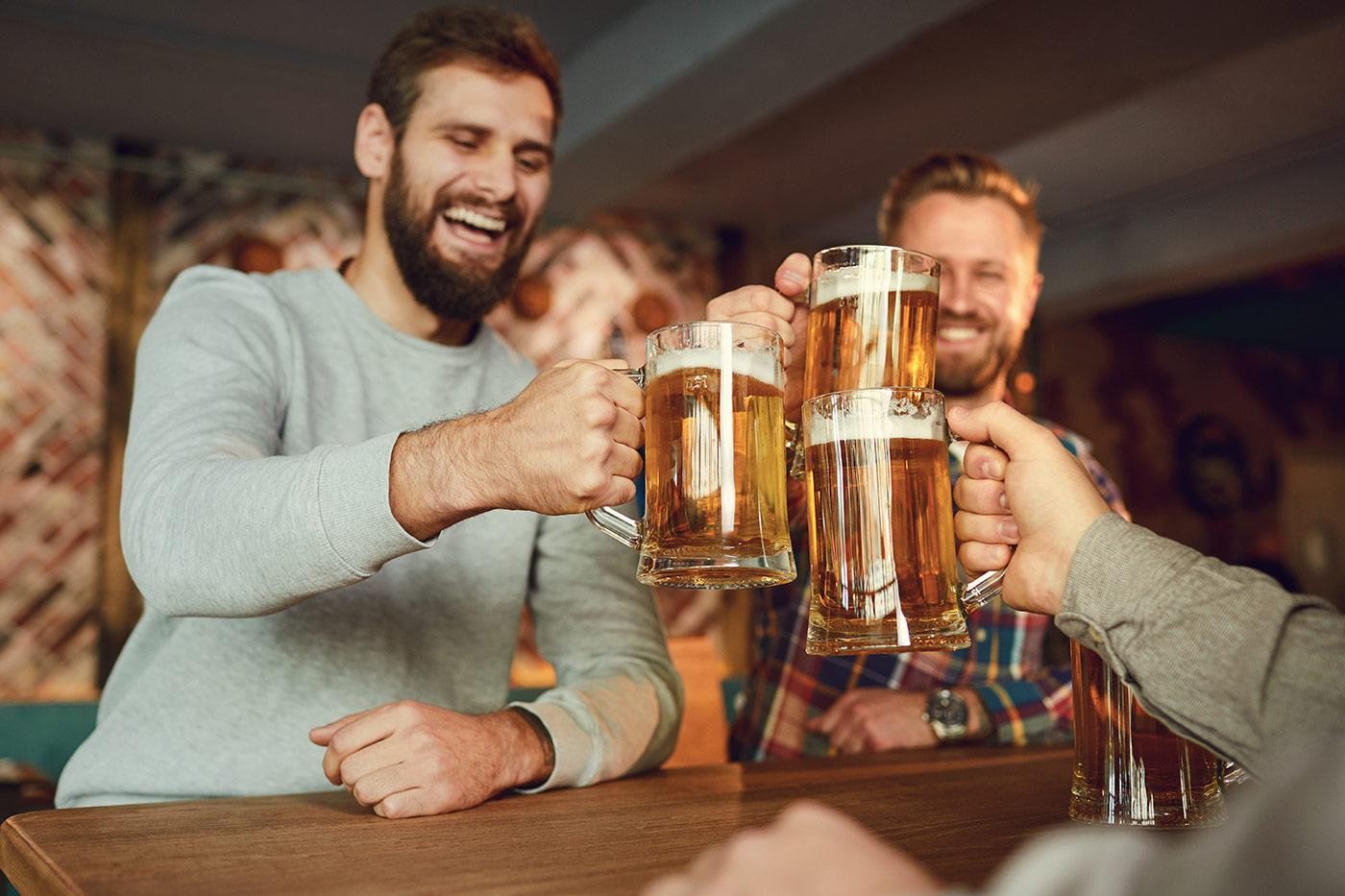 Group of happy friends clinking glasses with beer at a sports bar in a pub restaurant.