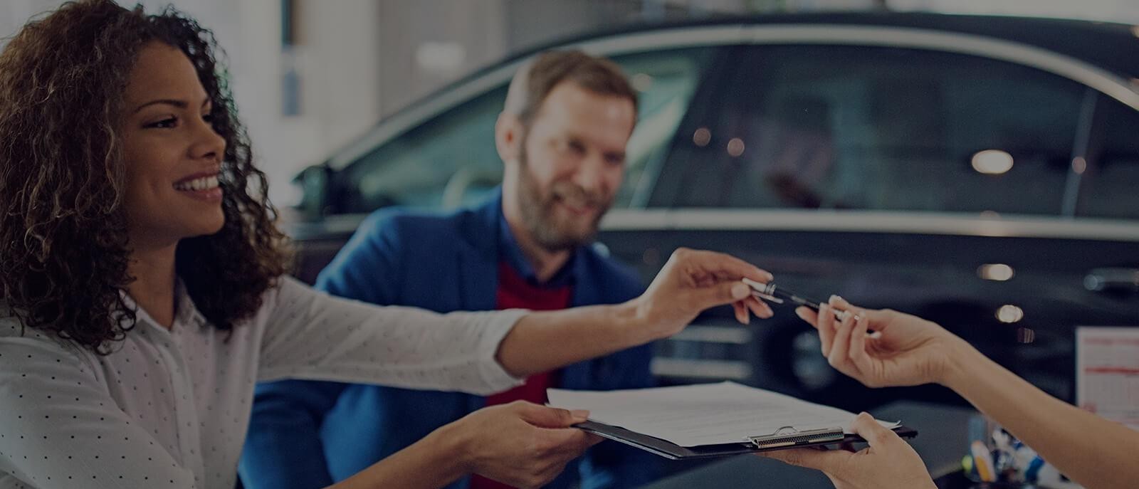 Smiling couple in a dealership, signing finance papers