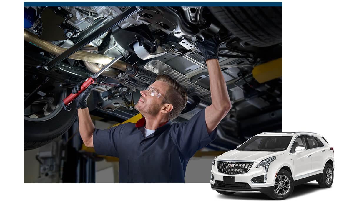White Cadillac XT5 with a service technician working on a vehicle in the background