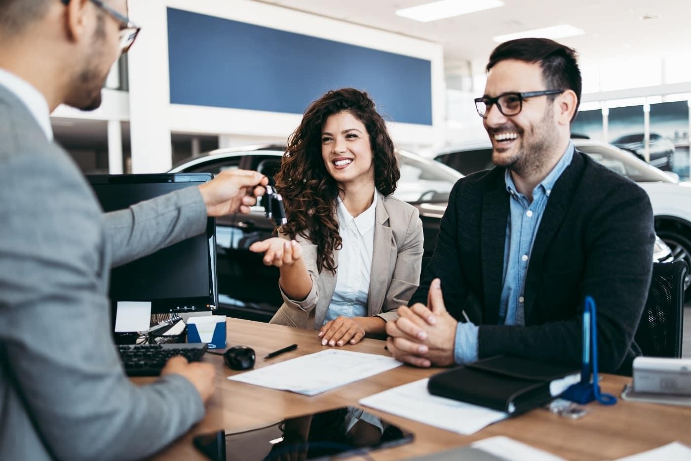 Happy couple reading buying plan with car salesperson