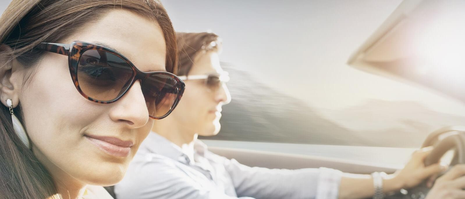 A couple driving along a sunny coastal road in a convertible.