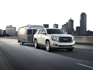 Silver 2018 GMC Yukon Towing Trailer on Highway with City Skyline in the Background